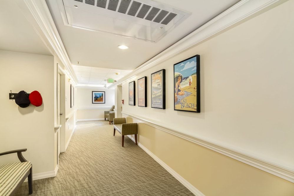 A well-lit hallway featuring framed artwork and chairs along a carpeted floor.