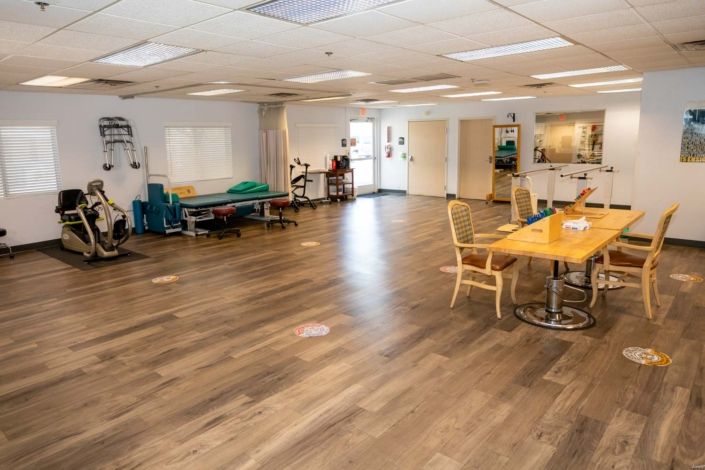 A spacious rehabilitation center room with therapy equipment and wooden flooring.