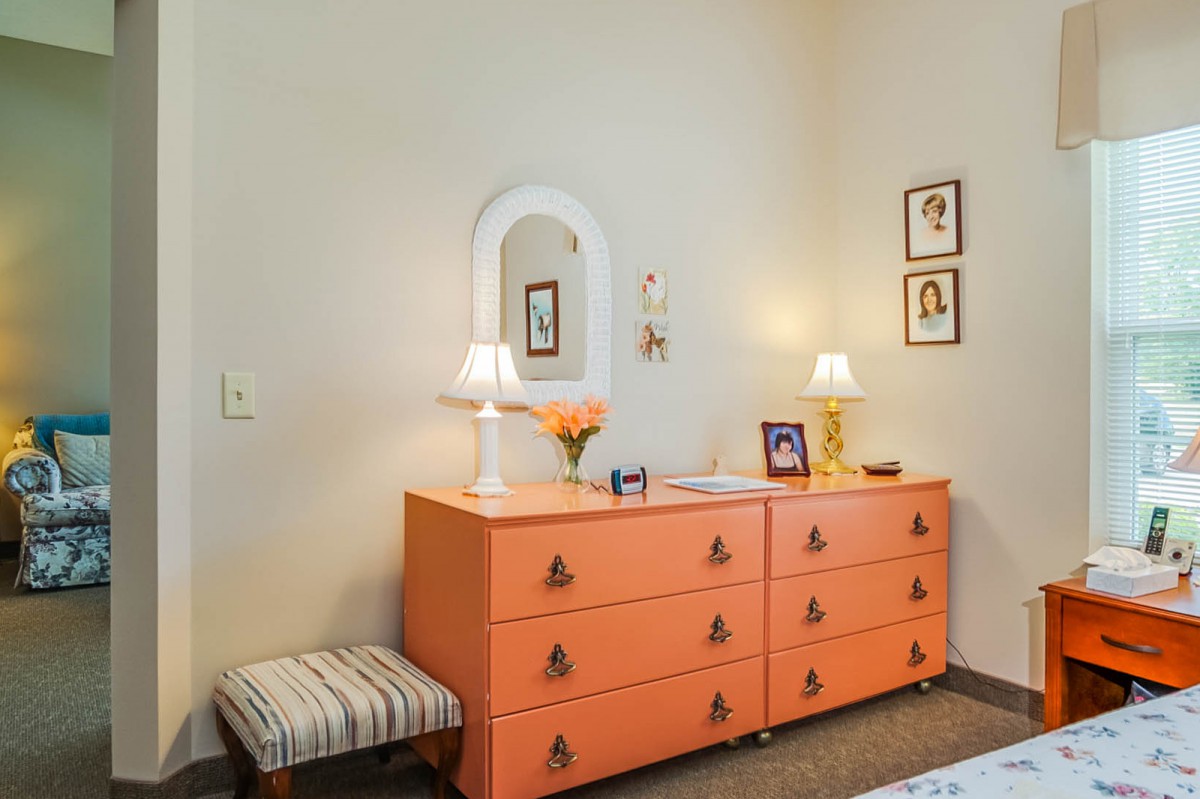 A cozy bedroom setting featuring an orange dresser with lamps and a mirror above, complemented by wall art and decor.