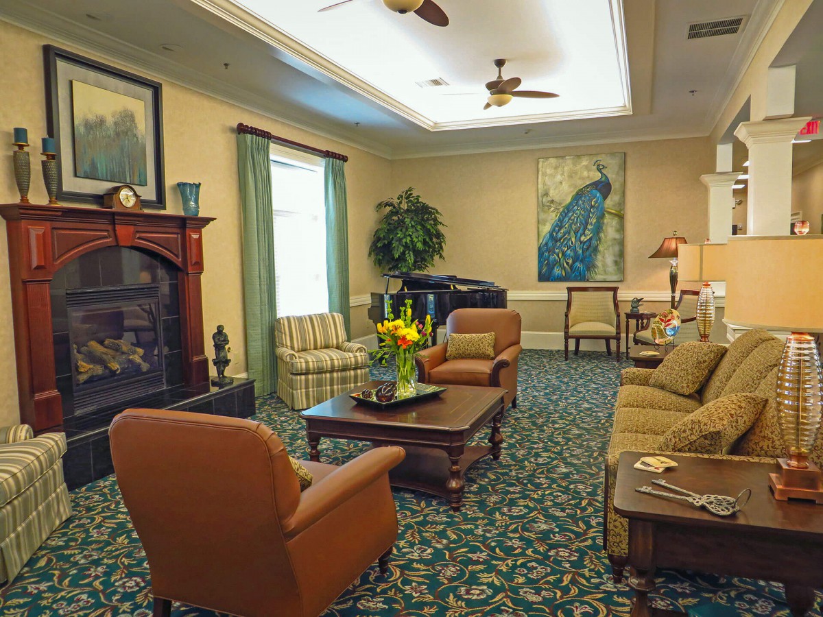 A cozy living room with elegant furniture and decor, featuring a fireplace, artwork, and plants.