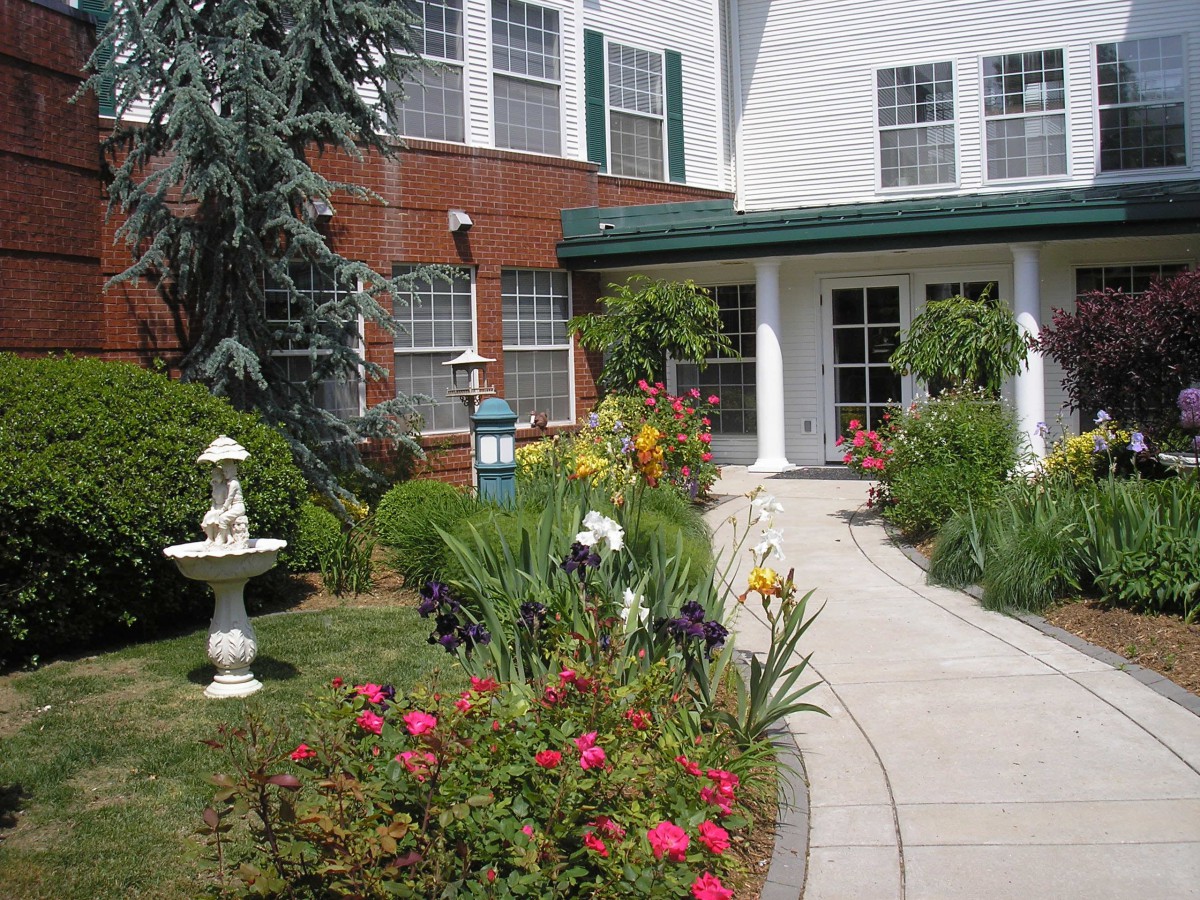 A beautifully landscaped garden with a variety of flowers and a small fountain, leading to the entrance of a building.