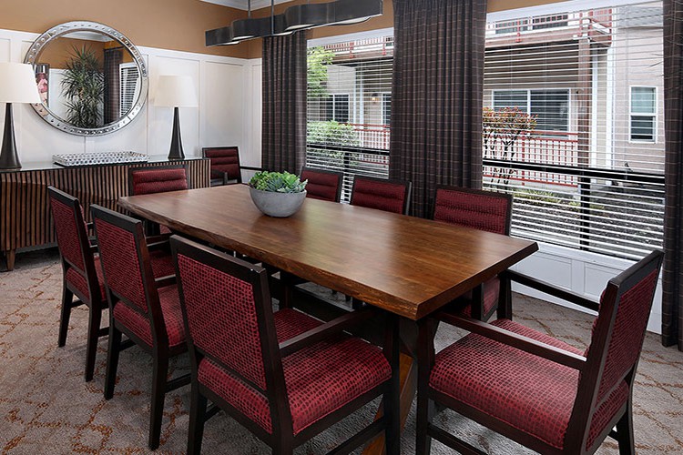 A dining room featuring a wooden table with red upholstered chairs and a plant centerpiece.