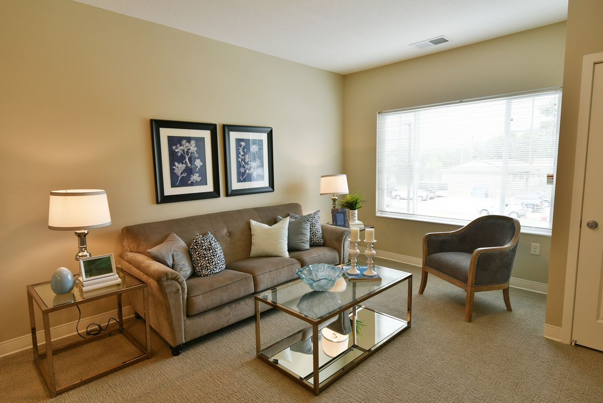 A cozy living room with a comfortable sofa, armchair, and glass coffee table, decorated with artwork and lamps.