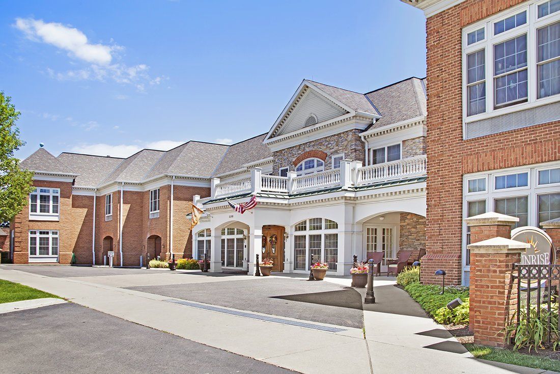A large brick residential building with a grand entrance and landscaped surroundings under a clear blue sky.