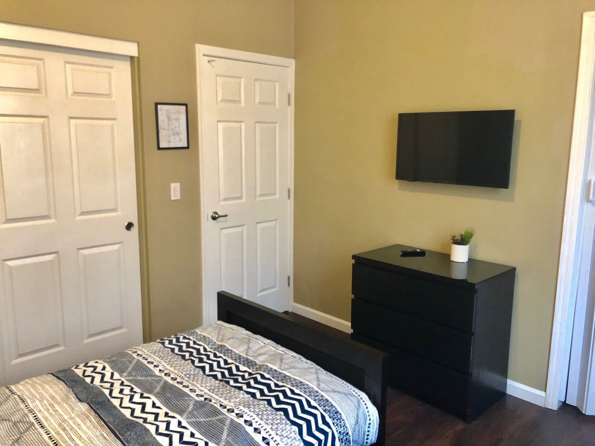 A minimalist bedroom with a bed, TV mounted on the wall, and a dresser.