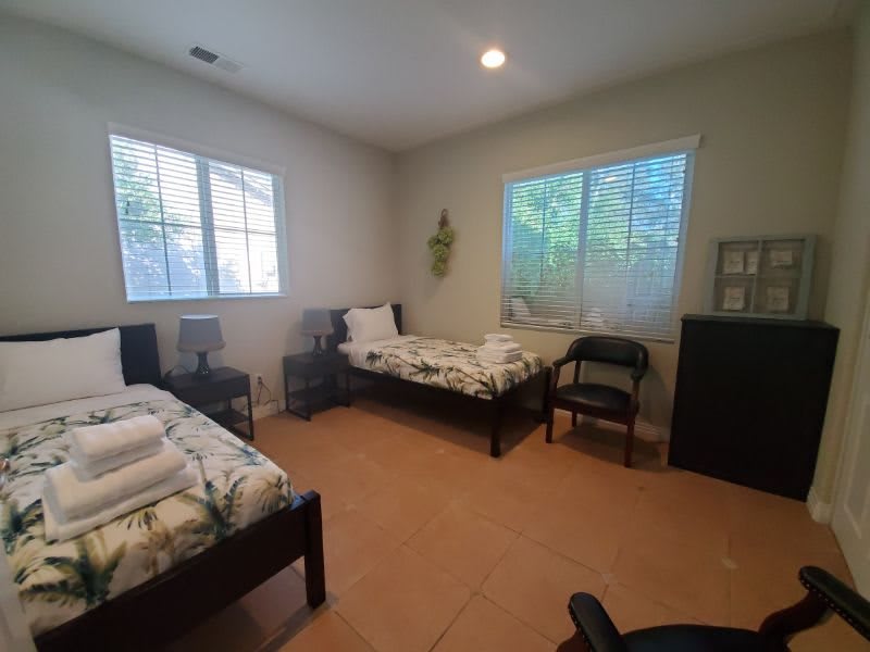 A cozy bedroom with two beds, ample natural light through the windows, and minimalistic decor.