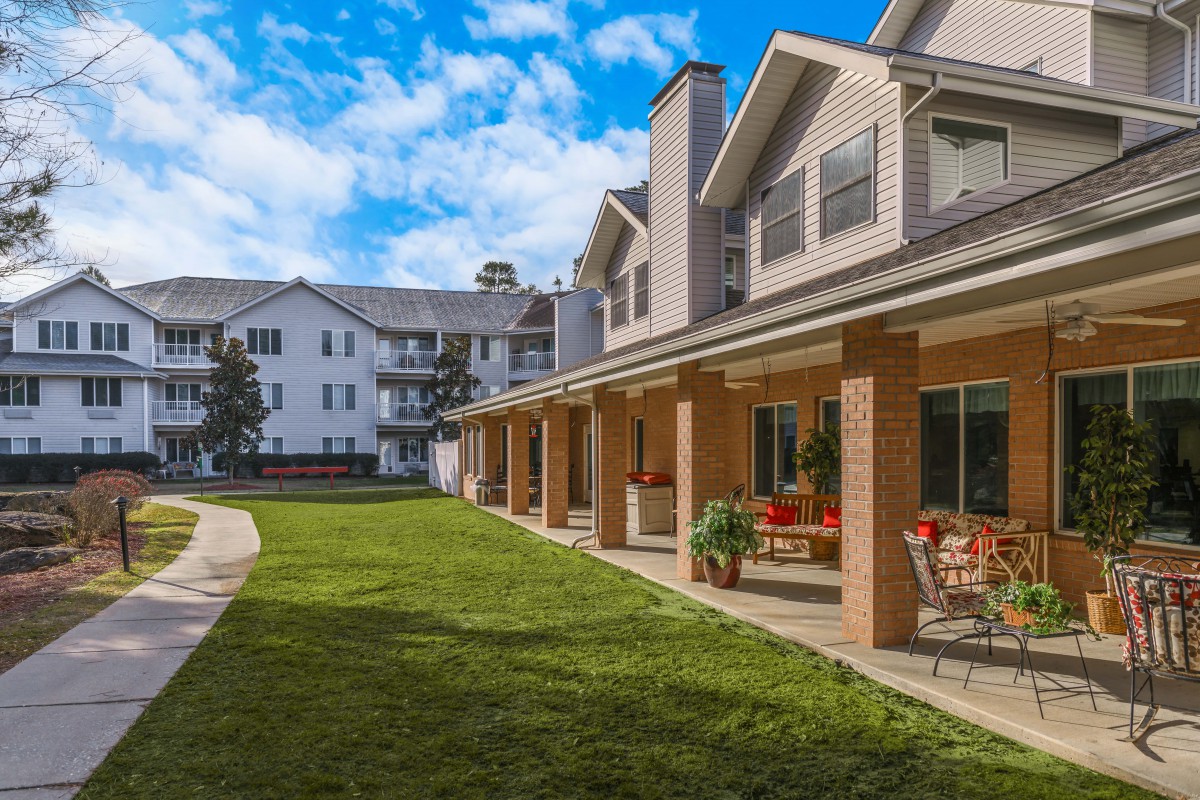 Exterior view of a residential building with a patio and green lawn under a blue sky.