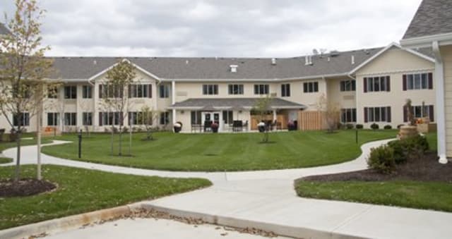 A two-story residential building with a well-maintained lawn and surrounding sidewalks under a cloudy sky.