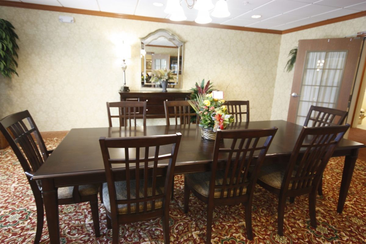 A formal dining room with a large wooden table, matching chairs, and decorative elements like flowers and a mirror.