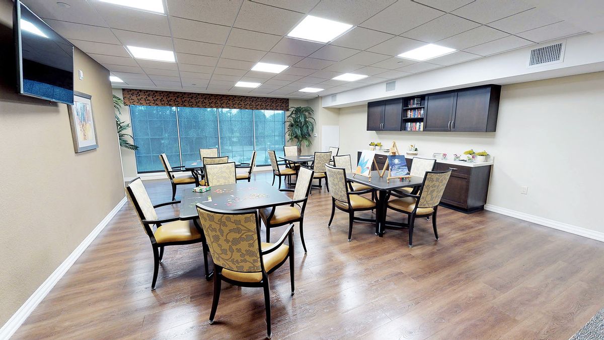 A modern dining area with several tables and chairs, featuring large windows and a kitchenette.