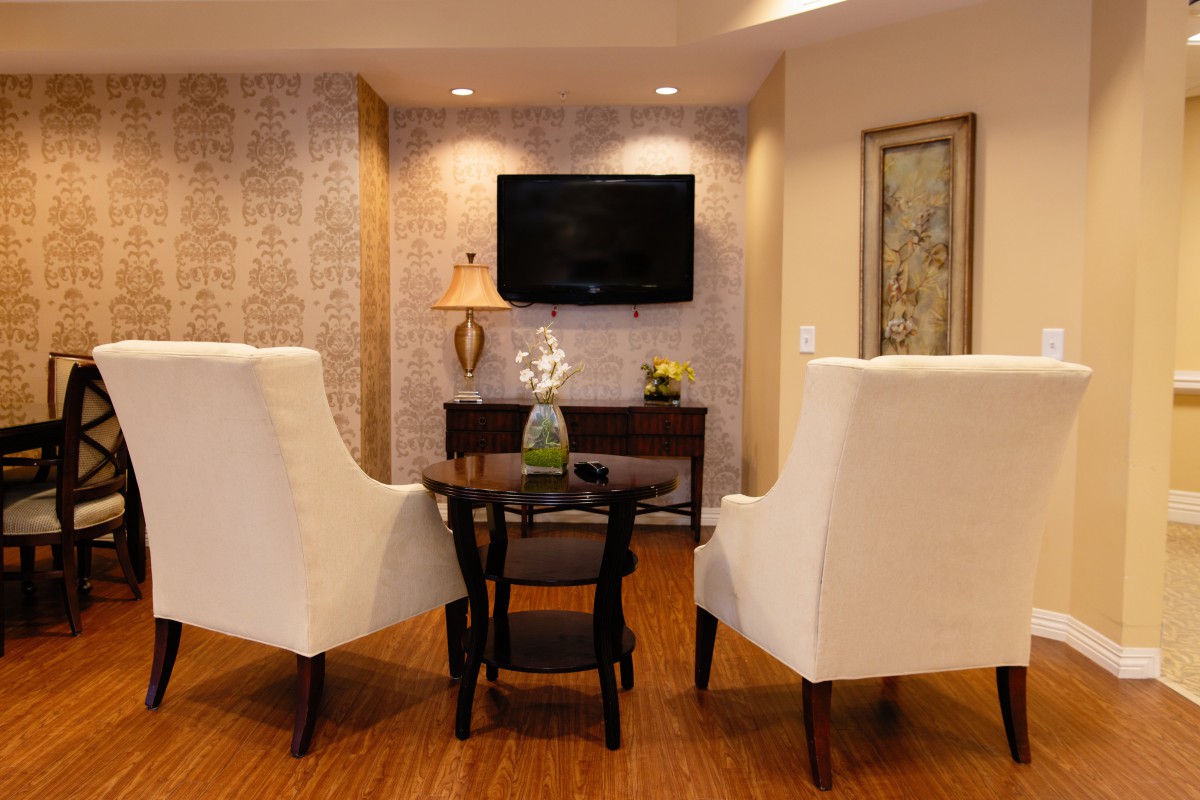 A cozy living room setup featuring two elegant chairs and a small wooden table, with a wall-mounted television and artistic decor.