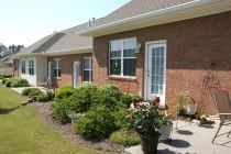 A well-maintained garden in front of a brick house with large windows and French doors.