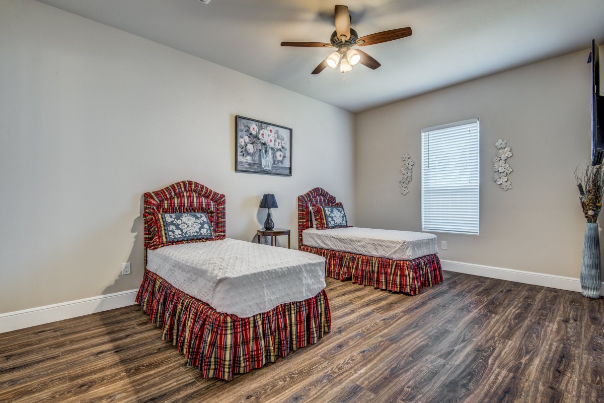 A neatly arranged bedroom with two twin beds, a wooden floor, and a ceiling fan.
