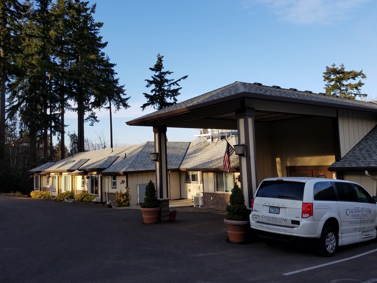 A view of a motel with an adjacent parking lot and surrounded by tall trees.