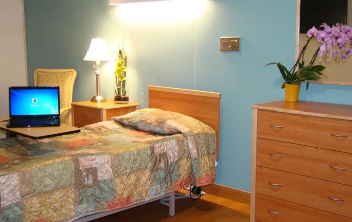 A cozy bedroom with a wooden bed and dresser, illuminated by a bedside lamp.