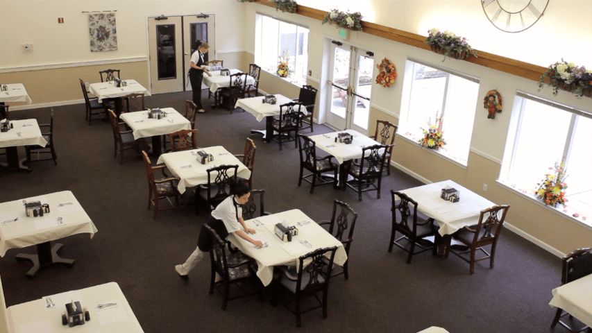 A clean dining area in a restaurant with tables neatly arranged and a waitstaff member attending to the setup.