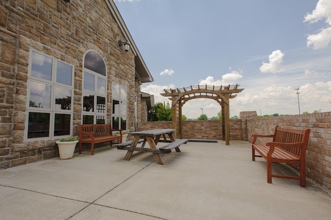 A stone patio with a picnic table and benches, featuring a pergola under a cloudy sky.
