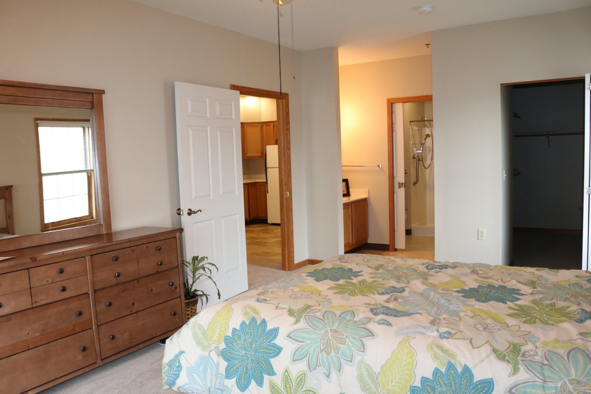A cozy bedroom featuring a floral comforter on the bed, a wooden dresser, and an open door leading to a hallway.