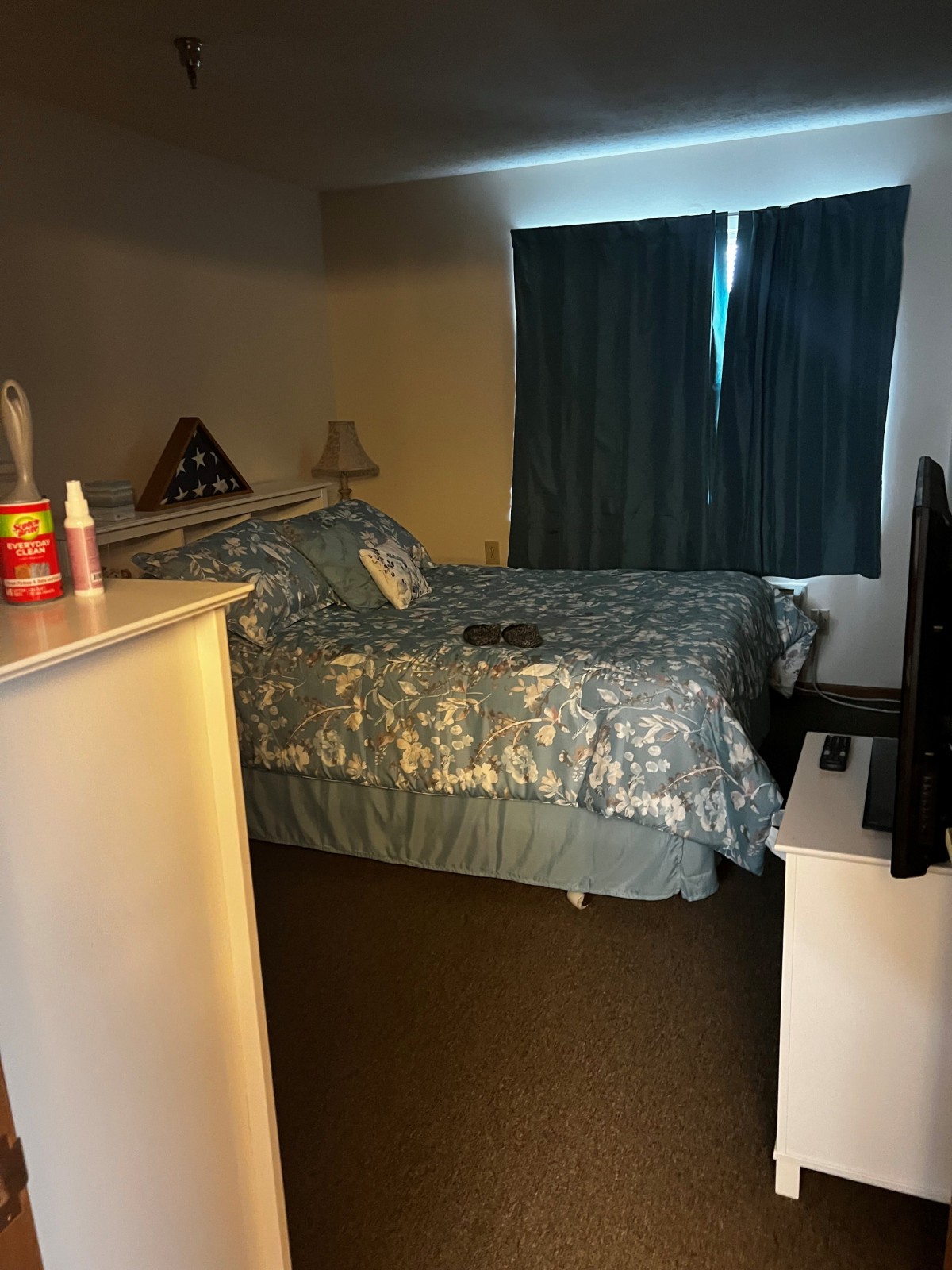 A cozy bedroom with a patterned bedspread, closed curtains, and a television on a stand.
