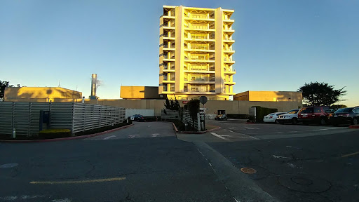 A modern apartment building bathed in sunlight, with a parking area in the foreground.