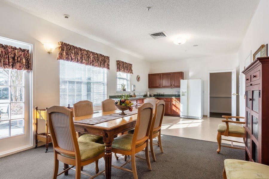 A cozy dining area connected to a small kitchen, featuring a wooden table and chairs with ample natural light.