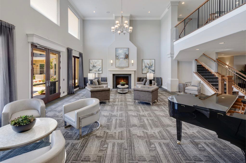 A spacious and luxurious living room with modern furnishings, featuring a fireplace, chandelier, and grand piano.