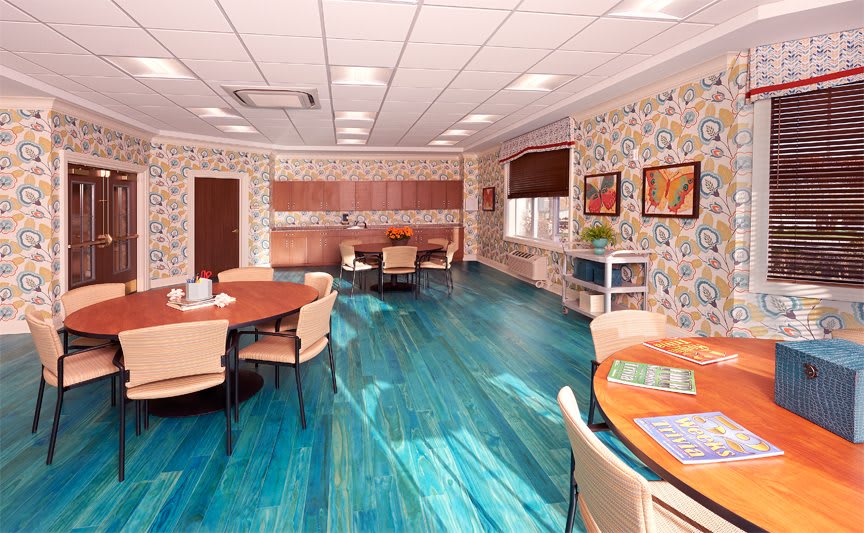 A cozy dining area with round tables, comfortable chairs, and vibrant wooden flooring.