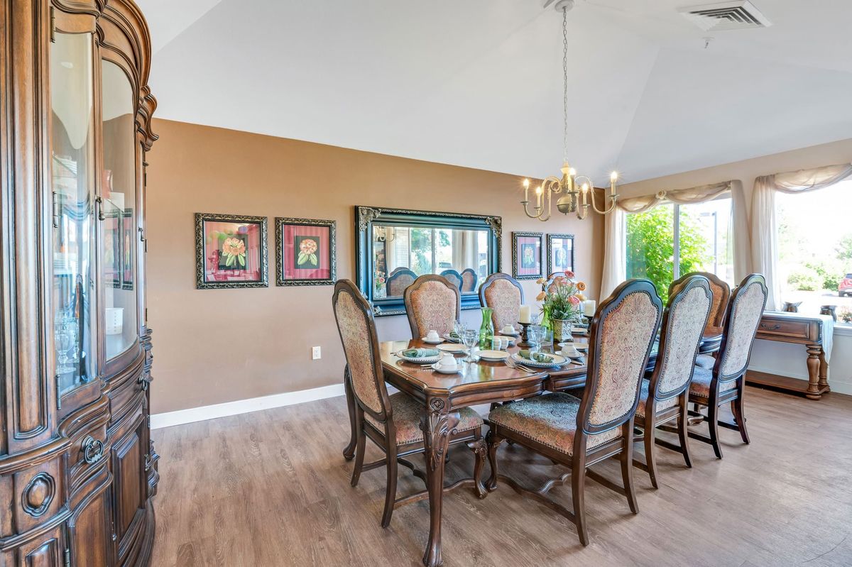 A spacious dining room with elegant chairs and a large table, adorned with a chandelier and wall decor.