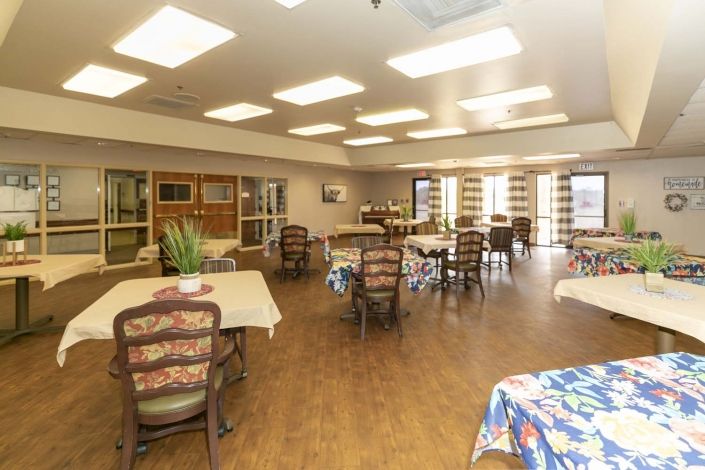 A well-lit dining area with multiple tables and chairs, featuring large windows and wooden flooring.