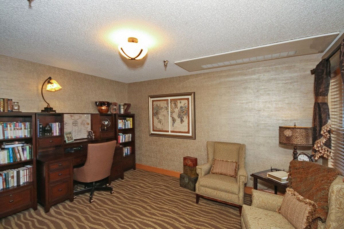 A cozy home office with a desk, armchairs, bookshelf, and wall map.