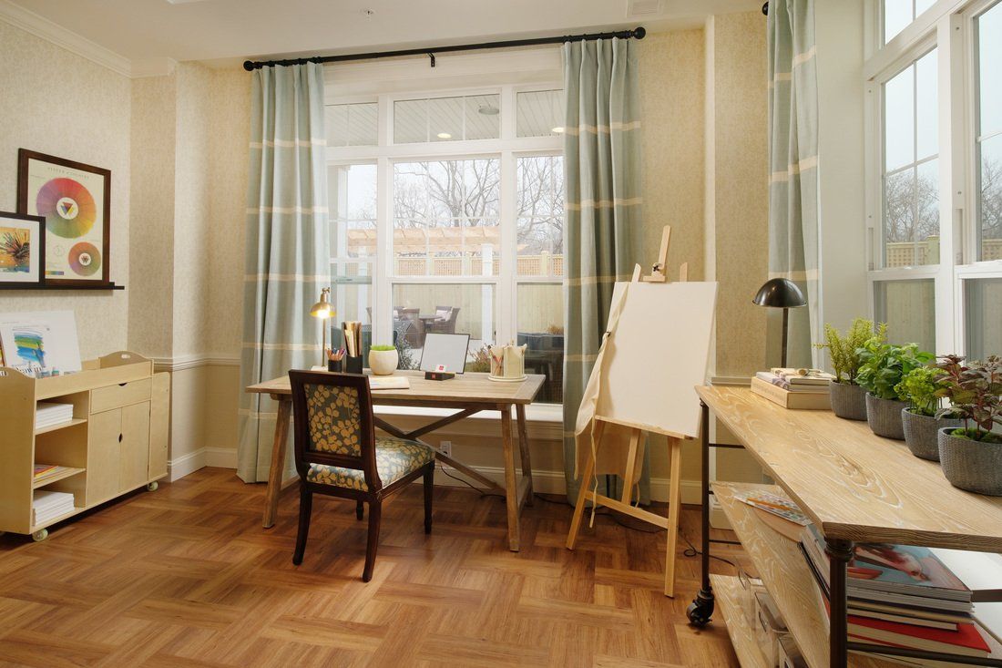 A cozy home office with an art easel by the window, featuring a desk, chair, and soft curtains.
