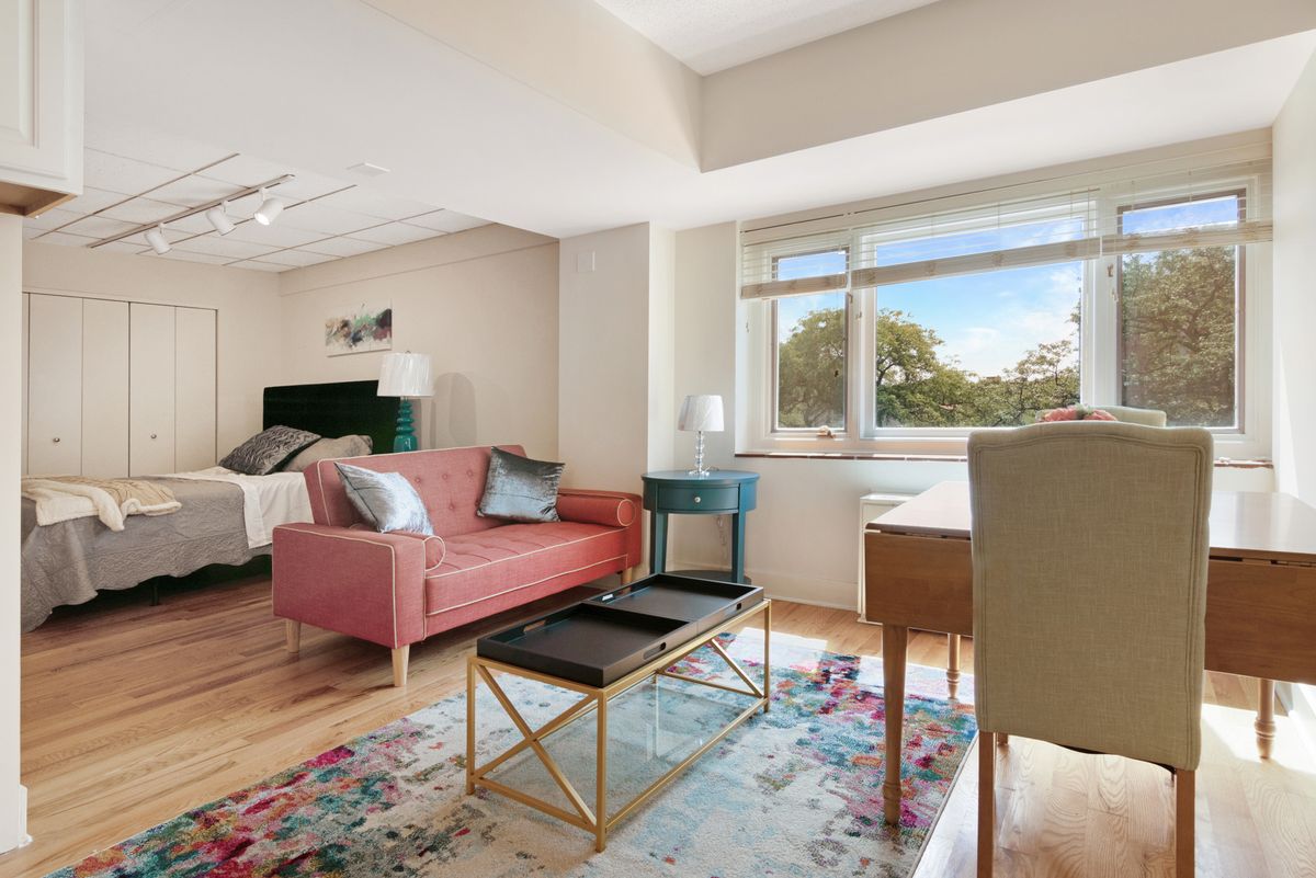A modern apartment living room featuring a pink sofa, colorful rug, and natural light from a large window.