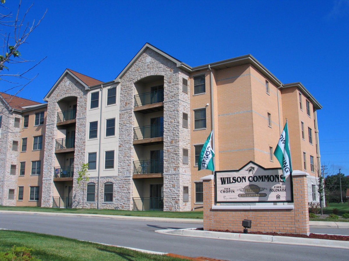A modern apartment building with a welcoming entrance sign and neatly landscaped surroundings.