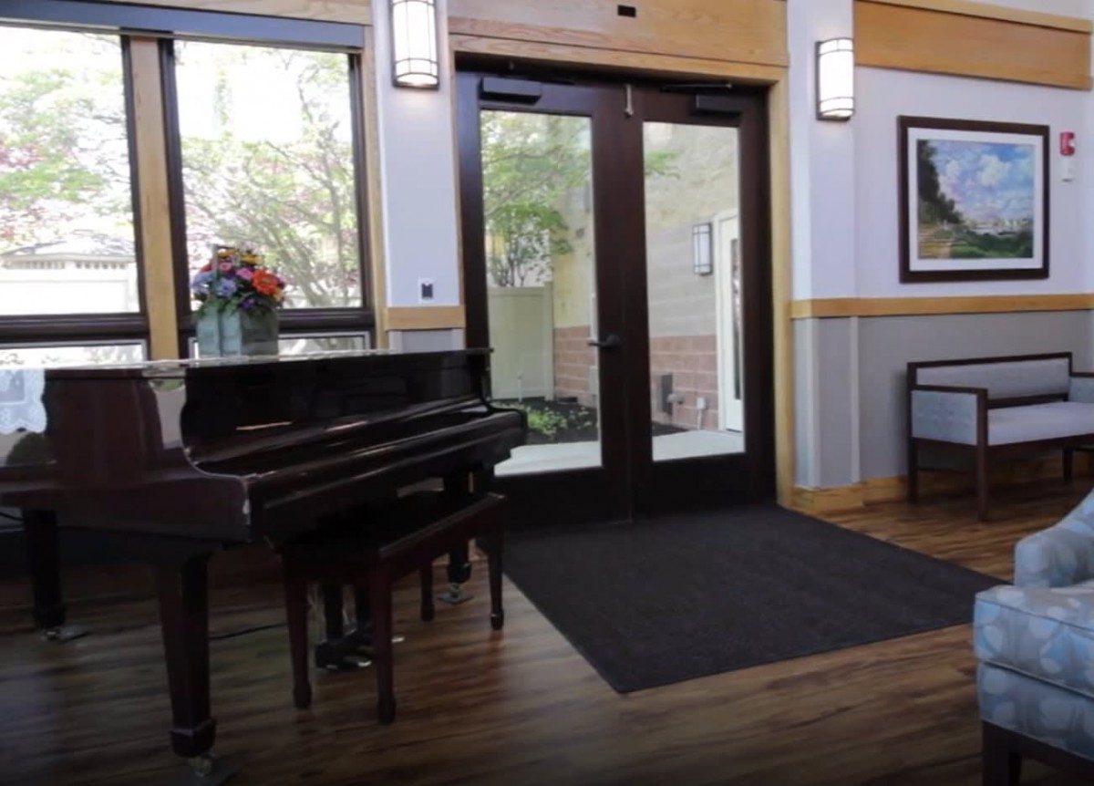 A bright lobby featuring a grand piano near the entrance with glass doors and natural light.