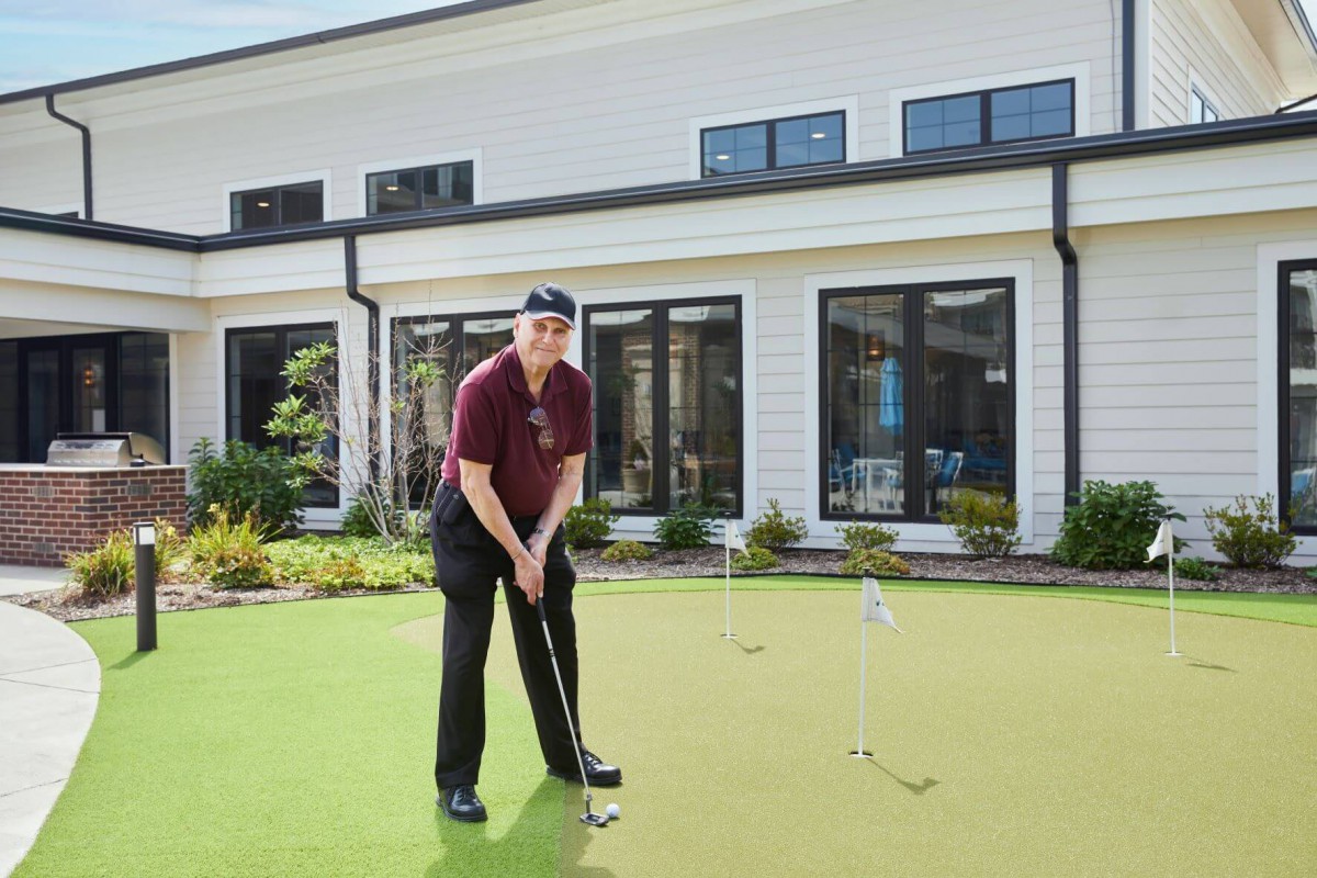 A person playing golf on a putting green in front of a house.