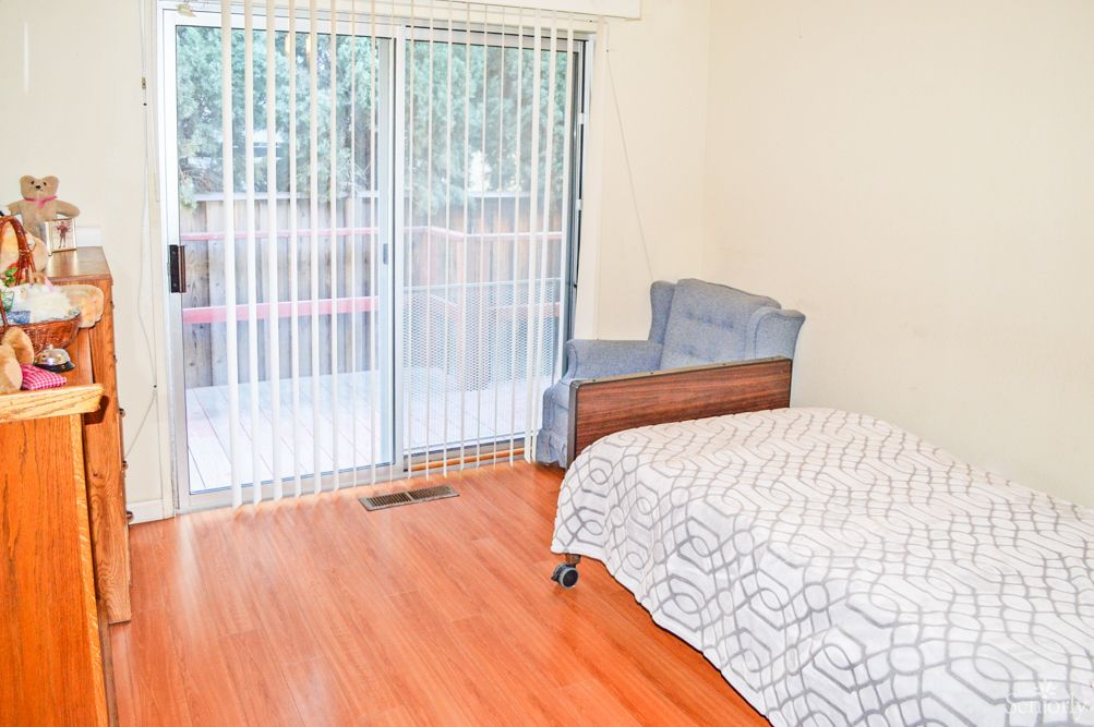 A bright bedroom with a single bed, wooden flooring, and a sliding glass door leading outside.