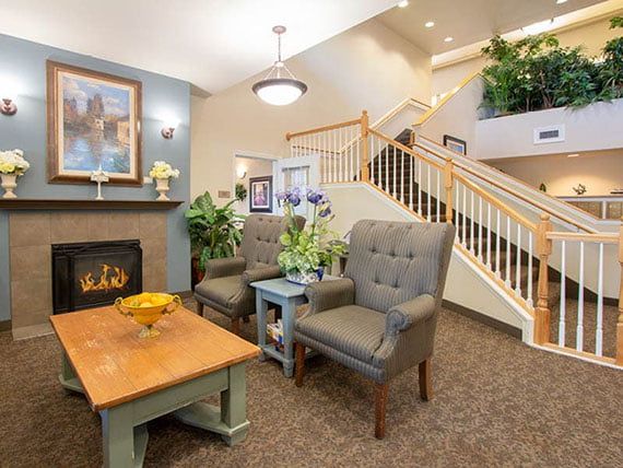 A cozy living room with a fireplace, comfortable armchairs, and a staircase leading to an upper level.