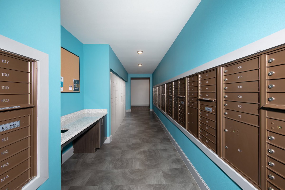 A modern mailroom with blue walls and multiple mailboxes along the hallway.