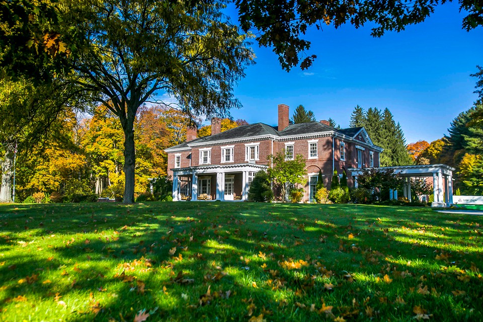 A brick mansion surrounded by autumn foliage on a bright, sunny day.