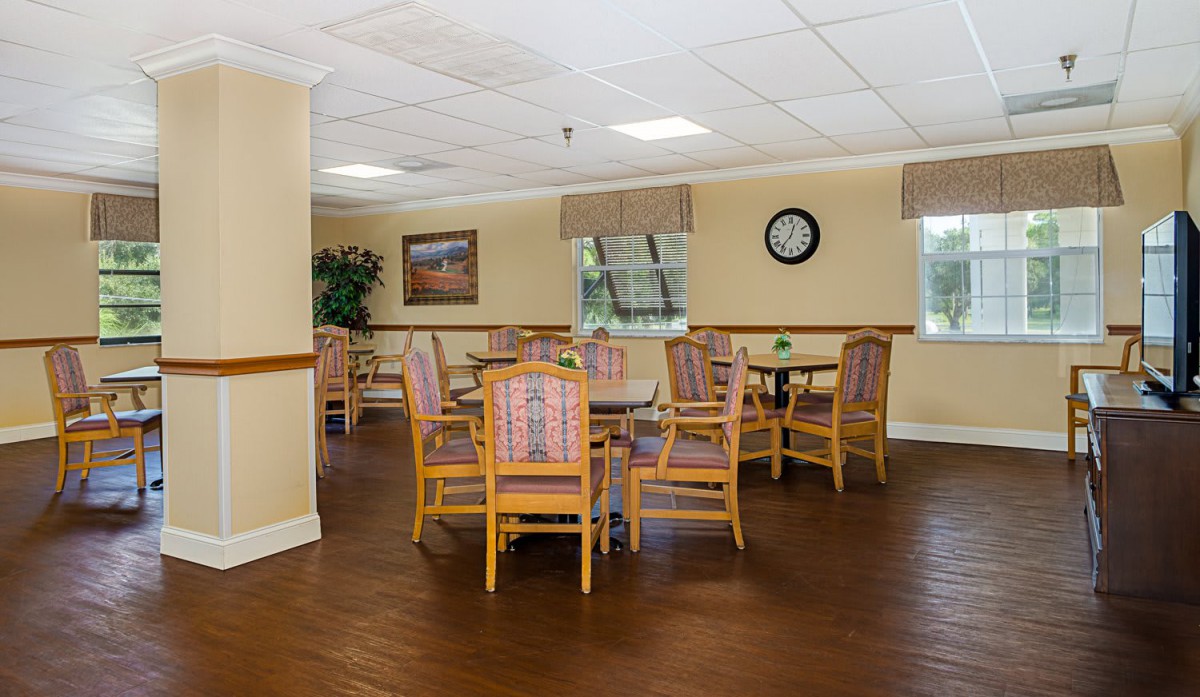 A well-lit dining area with wooden tables and chairs, decorated with artwork and a wall clock.
