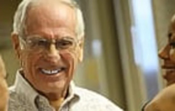 A smiling elderly man wearing glasses indoors.