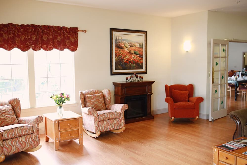 Cozy living room with armchairs and a fireplace, adorned by a painting and natural light streaming through the window.