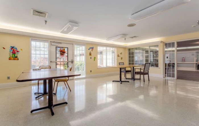 A bright, empty room with tables and chairs arranged near large windows.