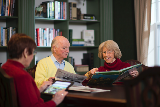 A group of elderly individuals enjoying a moment together while reading and discussing books at a cozy indoor setting.