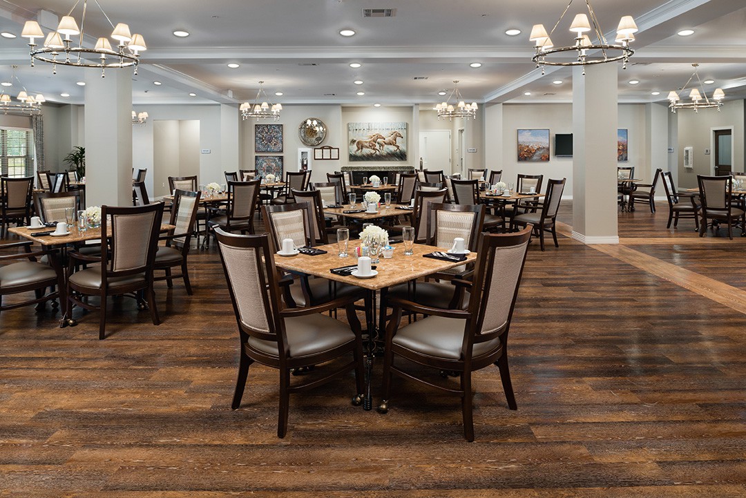 An elegant restaurant dining room with neatly arranged tables and chairs, wooden flooring, and chandeliers.