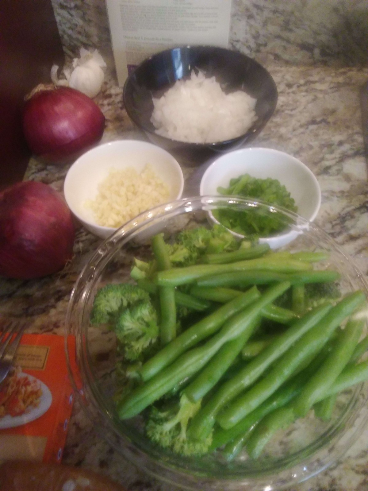 A selection of fresh cooking ingredients including onions, garlic, herbs, and green beans on a kitchen counter.