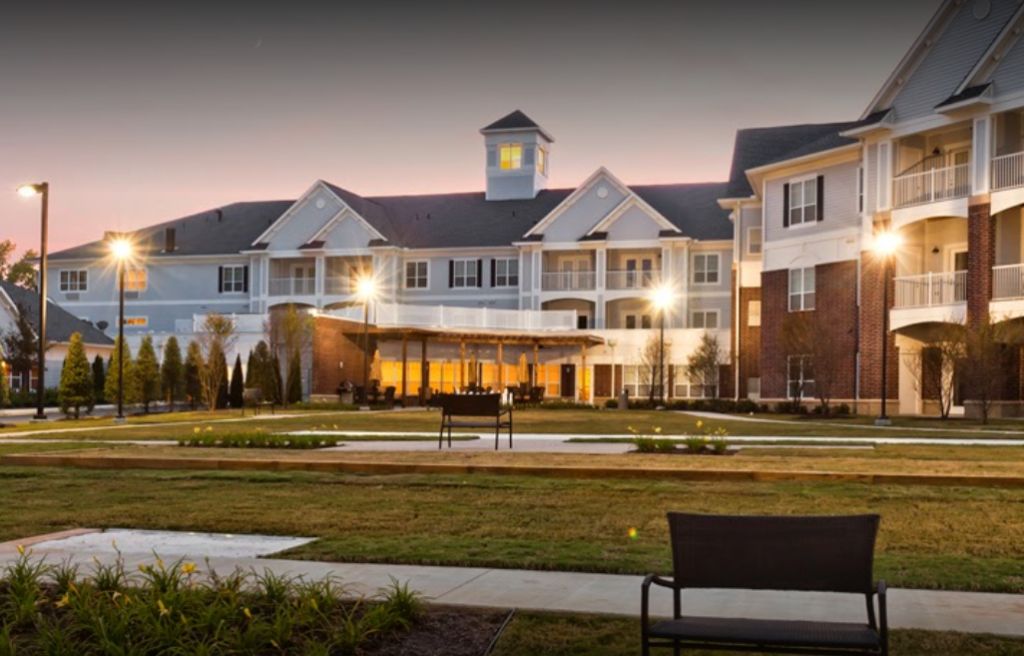 A beautifully lit building at dusk with landscaped grounds and a bench in the foreground.