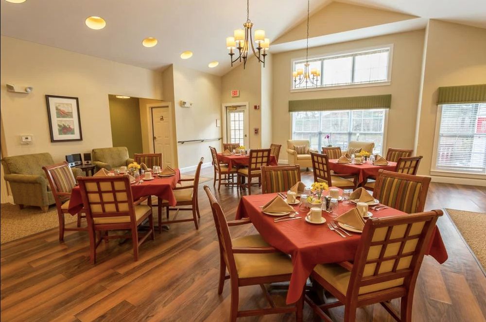 A cozy dining room with neatly arranged tables and chairs, set for a meal under elegant chandeliers.