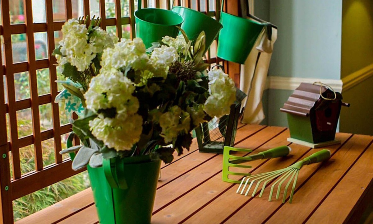 A wooden table adorned with a vase of flowers, green watering cans, and gardening tools.