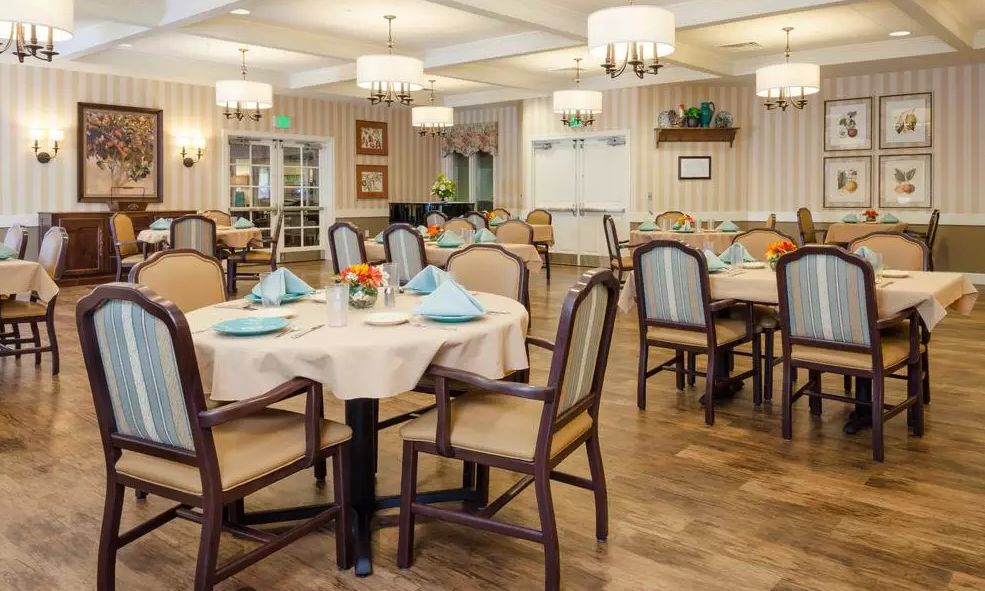 An elegantly set dining room with neatly arranged tables and chairs, accentuated by chandeliers and tasteful decor.